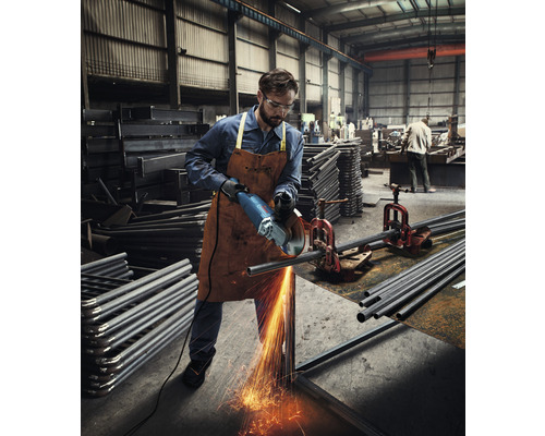 Dělník řeže kovovou trubku úhlovou bruskou v dílně.