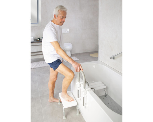 Muž používá zvedák do vany a sedátko do vany v světlé koupelně.