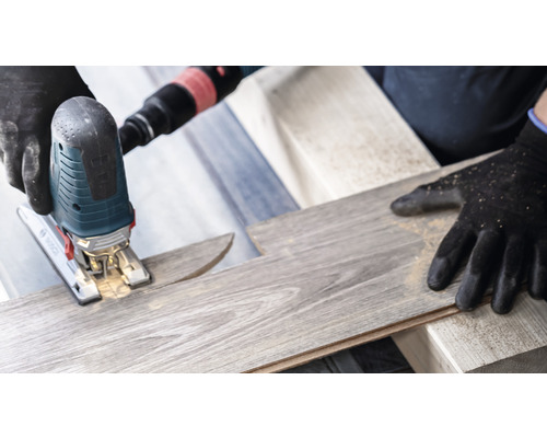 Přímočará pila řeže laminátovou desku. Používají se ochranné rukavice.