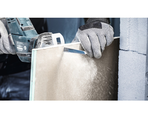 Osoba řeže sádrokartonovou desku pilou.