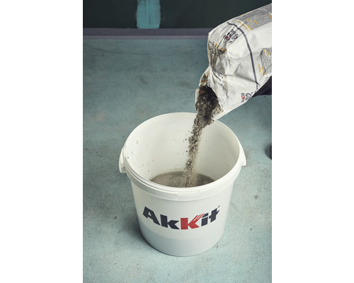 Osoba sype suchou betonovou směs z pytle do kbelíku.