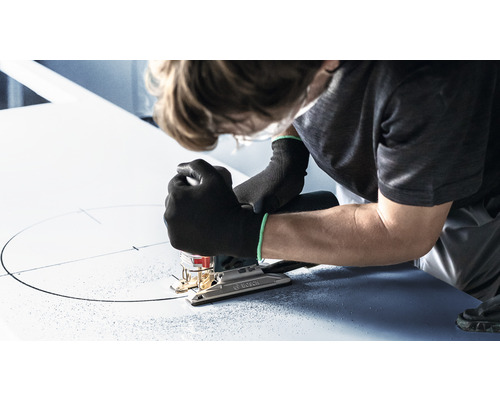 Osoba vyřezává kruh do desky pomocí přímočaré pily.