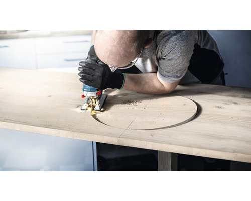 Muž vyřezává otvor do dřevěné desky pomocí přímočaré pily.