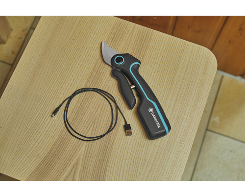 Akumulátorové zahradní nůžky Gardena s USB nabíjecím kabelem na dřevěném stole