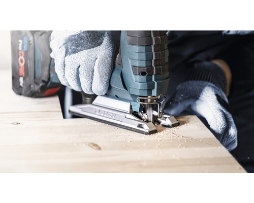 Osoba řeže dřevo přímočarou pilou a má na sobě rukavice