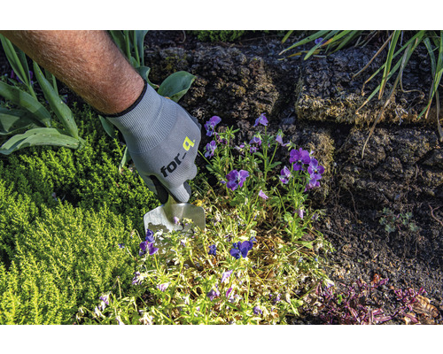 Osoba v zahradních rukavicích pracuje se sázecí lopatkou na zahradním záhonu.