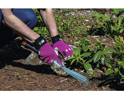 Osoba hráběmi shrabuje zahradní odpad a chrání ji zahradní rukavice.