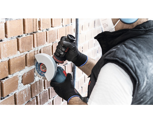 Řemeslník řeže cihlovou zeď úhlovou bruskou