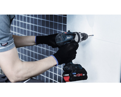 Muž vrtá vrtačkou díru do zdi.