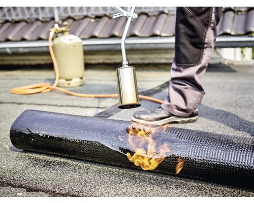 Pokrývač svařuje asfaltový pás plynovým hořákem na střeše.