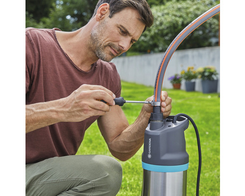 Muž připevňuje zahradní hadici šroubovákem k čerpadlu Gardena.