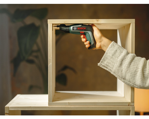 Osoba montuje dřevěnou polici pomocí akumulátorového šroubováku značky Bosch.