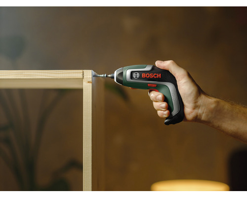 Osoba šroubuje šroub do dřevěné desky pomocí akumulátorového šroubováku Bosch.