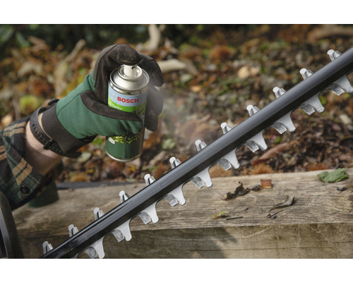 Osoba stříká čepel nůžek na živý plot údržbovým sprejem Bosch.