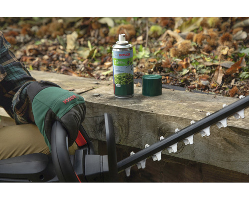 Logo Bosch. Osoba se zahradními rukavicemi a nůžkami na živý plot vedle spreje pro údržbu nůžek na živý plot na dřevěném povrchu.