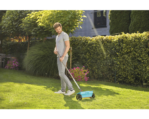 Muž používá rozmetadlo hnojiv na trávníku.