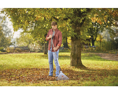 Muž s hráběmi na listí v zahradě, podzimní listí na trávníku.