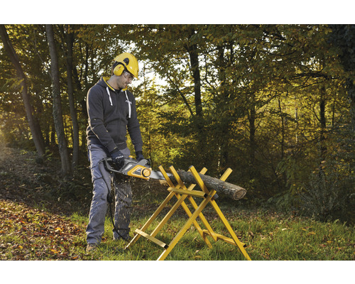 Muž řeže kus dřeva elektrickou pilou na kozě