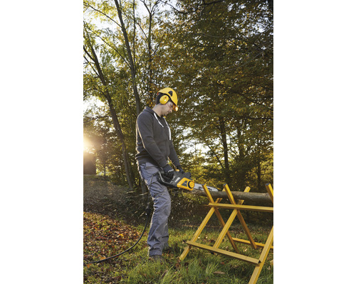 Muž řeže elektrickou pilou špalek dřeva na kozě na zahradě