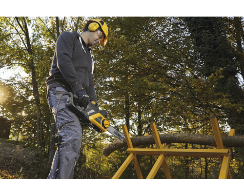 Muž řeže dřevo elektrickou pilou na kozlíku na zahradě.