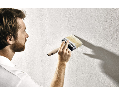 Muž maluje stěnu štětkou.