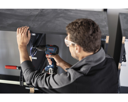 Řemeslník pracuje s akumulátorovým šroubovákem na kusu nábytku