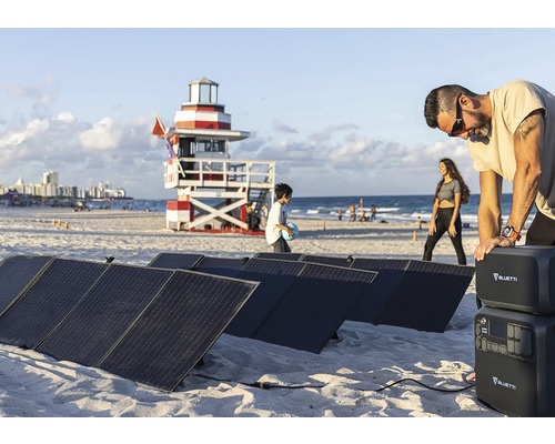 Solární panely a úložiště energie Bluetti na pláži s lidmi a záchrannou věží v pozadí