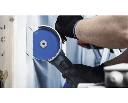 Osoba řeže s úhlovou bruskou sádrokartonovou stěnu.