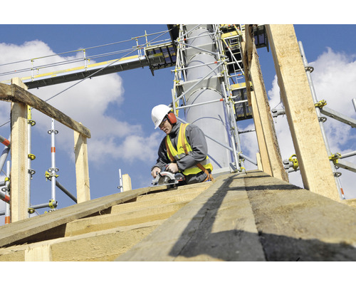 Stavební dělník řeže dřevěnou desku kotoučovou pilou na lešení.