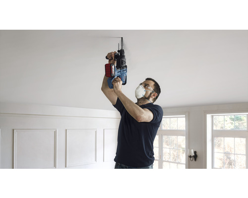 Muž vrtá vrtačkou díru do stropu.