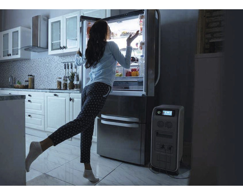 Žena stojí před lednicí vedle generátoru proudu v kuchyni.