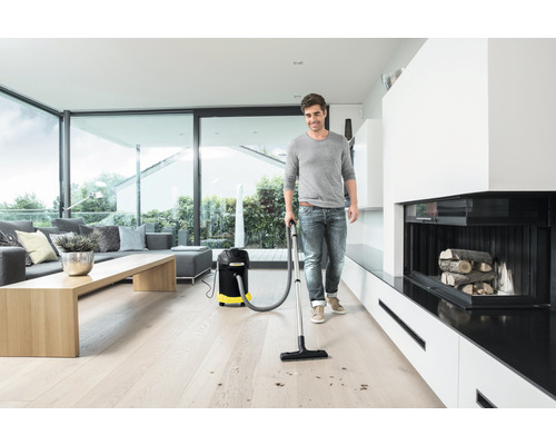 Muž vysává dřevěnou podlahu víceúčelovým vysavačem ve světlém obývacím pokoji