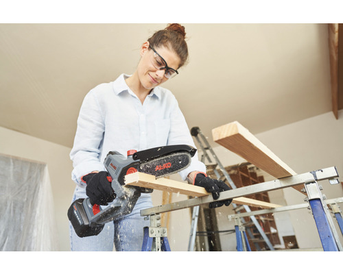 Žena řeže dřevo akumulátorovou řetězovou pilou AL-KO na pracovním stole