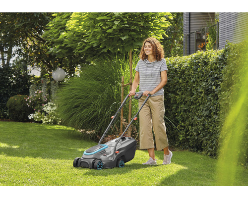 Žena obsluhuje sekačku na trávu na zahradě.
