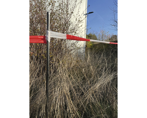 Výstražná páska na kovovém sloupku před keři a trávou