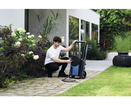 Muž připojuje vysokotlaký čistič na zahradě.