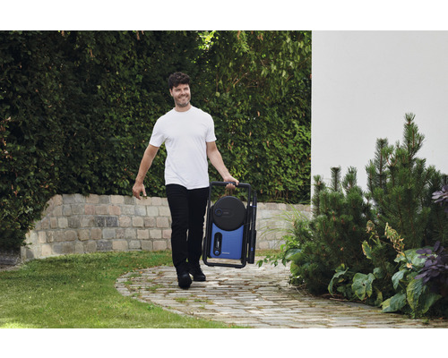 Muž nese přenosnou tlakovou myčku na zahradě.