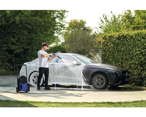 Muž myje auto vysokotlakým čističem na zahradě.