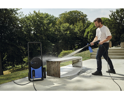 Muž čistí zahradní lavici venku pomocí vysokotlakého čističe.