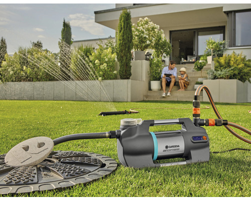 Domácí vodárna Gardena s příslušenstvím na zahradě, zatímco otec a dítě sedí na terase