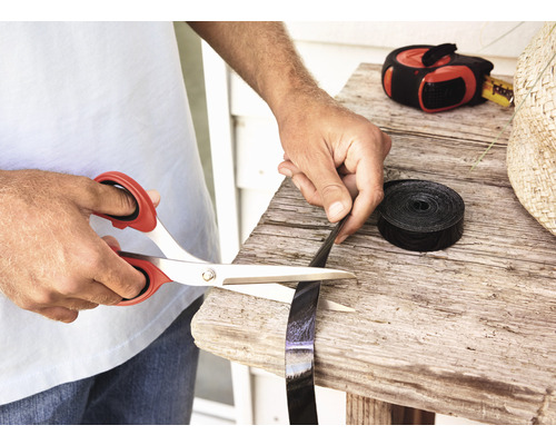 Osoba stříhá černou plastovou pásku nůžkami na dřevěném stole.