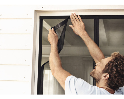 Muž instaluje do okna síť proti hmyzu