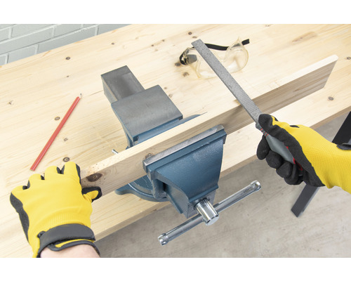 Pracovní stůl se svěrákem, dřevěný kus, pilník, tužka, ochranné brýle a pracovní rukavice