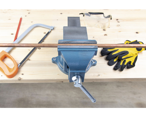 Pracovní stůl se svěrákem, měděná trubka, ruční pila, ochranné brýle a pracovní rukavice