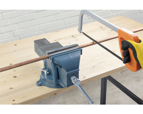 Svěrák drží měděnou trubku, která se řeže pilou na kov.