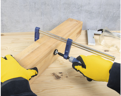 Utahování šroubové svěrky na dřevěné desce v rukavicích