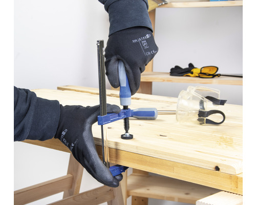 Osoba upevňuje obrobek jednou rukou svěrkou na dřevěném povrchu.