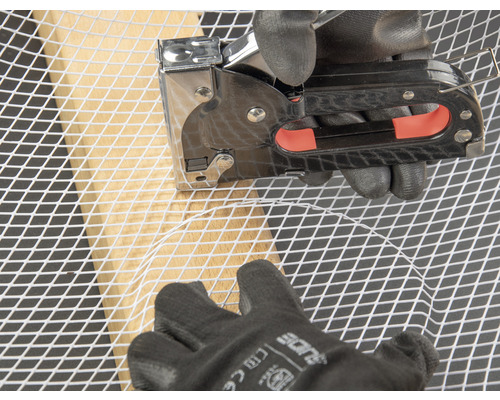 Osoba připevňuje drátěné pletivo k dřevěnému rámu sponkovačkou.