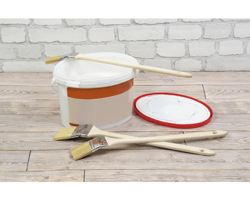 Kbelík s barvou, štětce a miska na barvu před cihlovou zdí