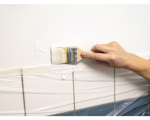 Osoba maluje štětcem stěnu nad dlaždicemi zakrytými fólií.